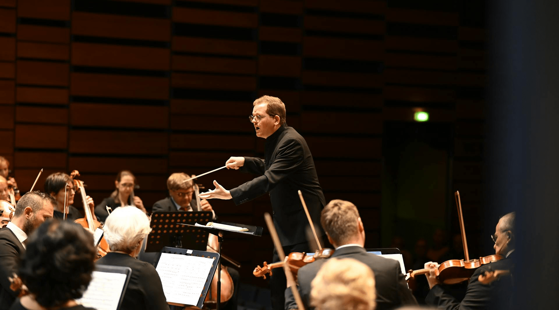 A conductor stands over the orchestra. Photo.
