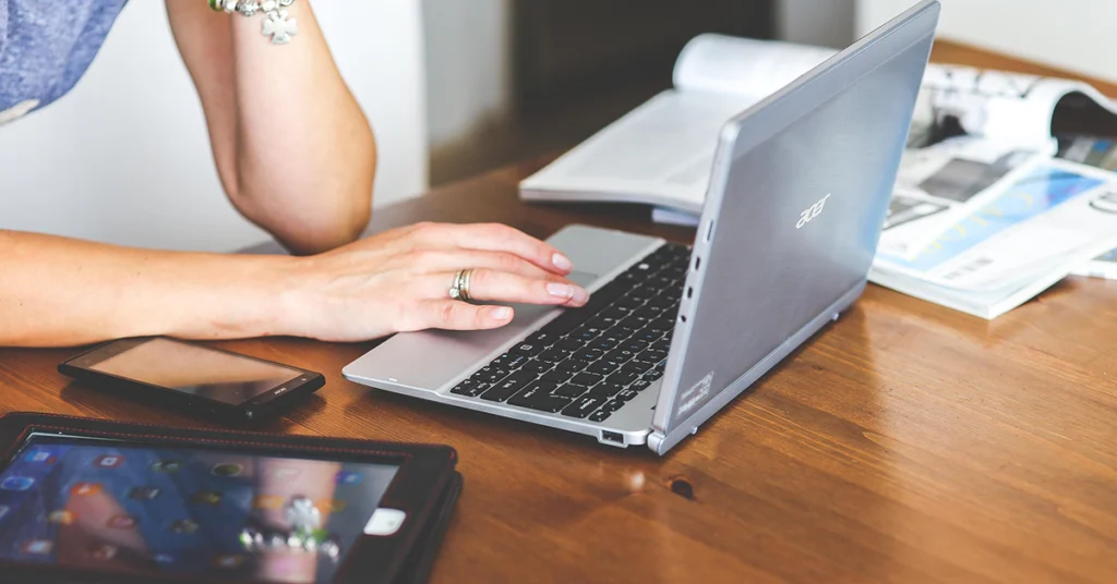 A woman sits at a taple, her laptop and ipad open.
