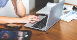 A woman sits at a taple, her laptop and ipad open.