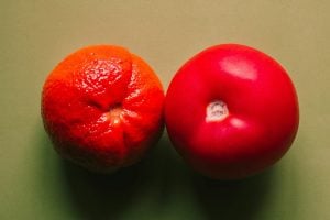 A photo of an apple and an orange side by side on a green background