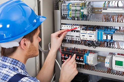 A technician with a blue hardhat probes a series of connectors in a panel with a multimeter