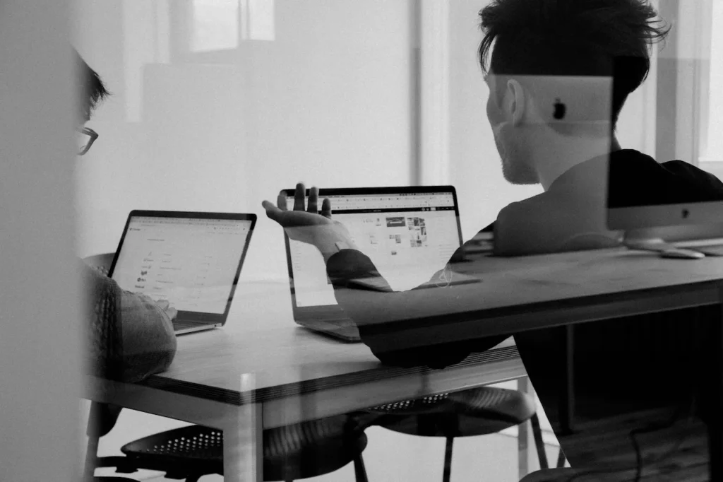 Two colleagues discussing work at laptops in office