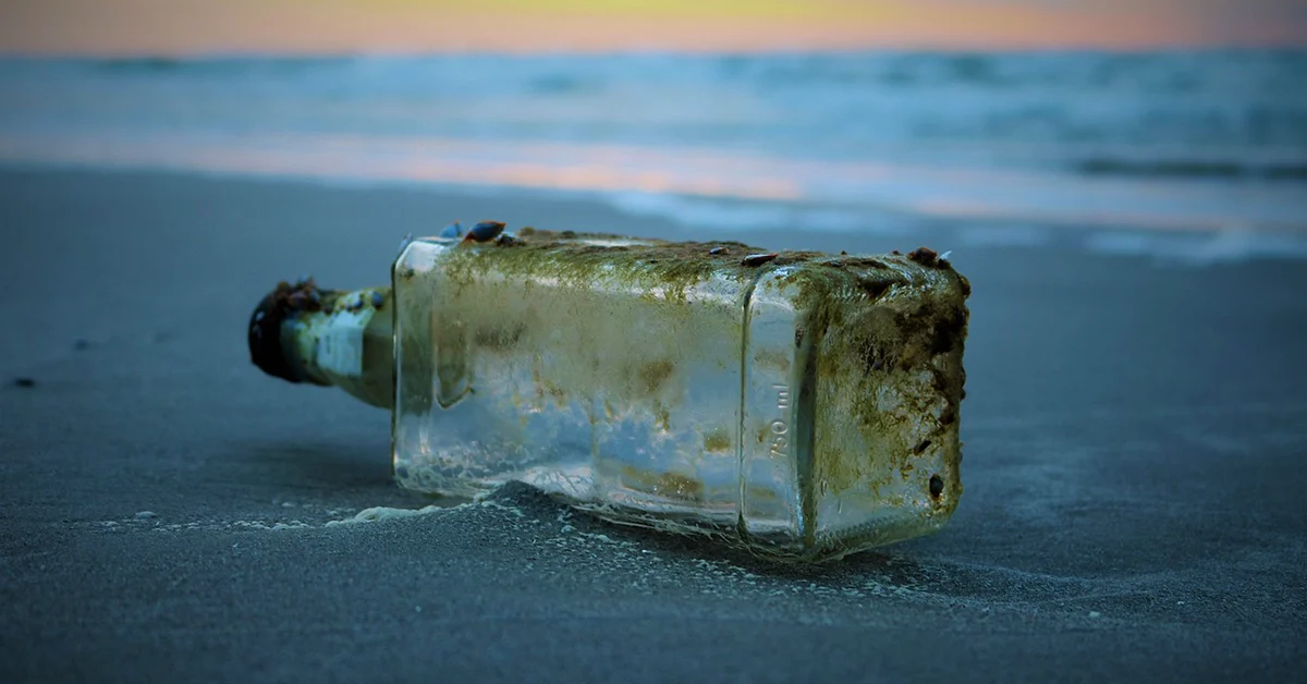 A photograph of an empty whisky bottle laying on a beach