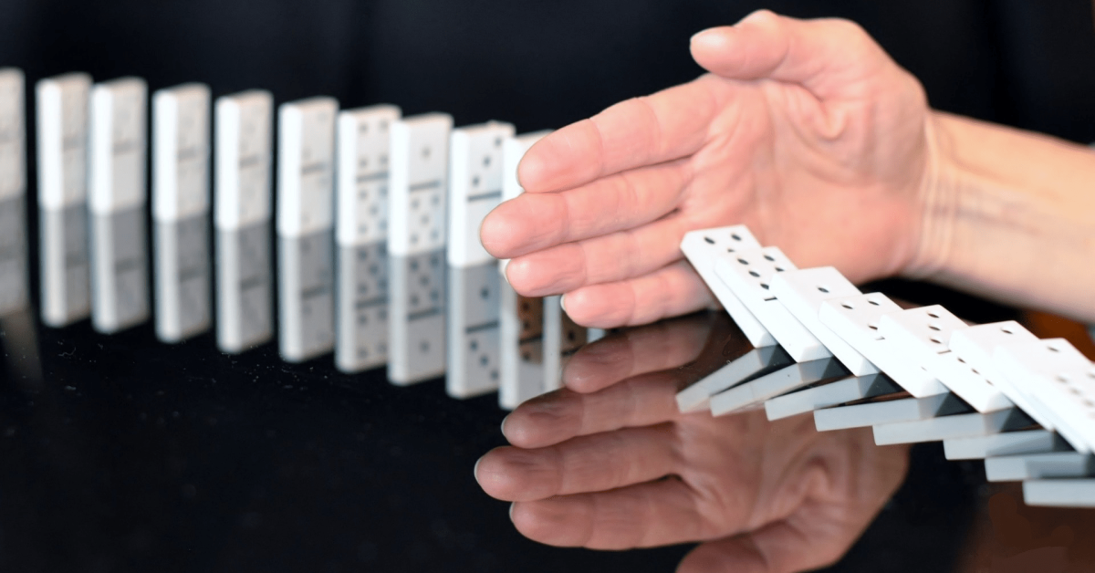 A hand blocks a series of falling dominoes from continuing on down the line.