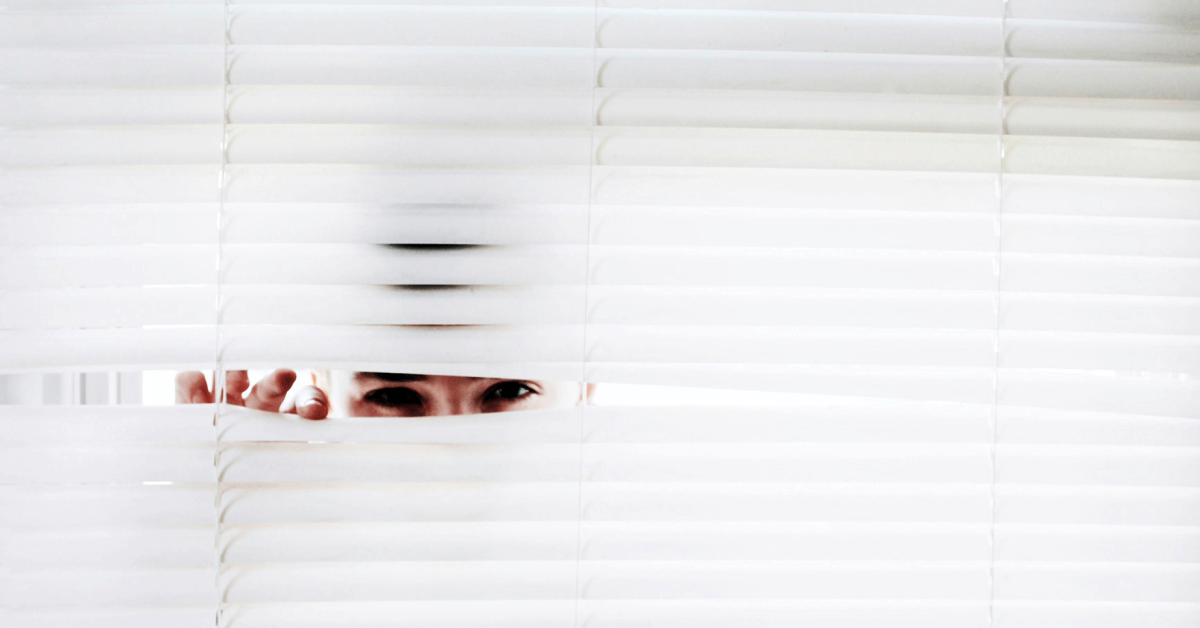 A photograph of a man peeking through vertical blinds