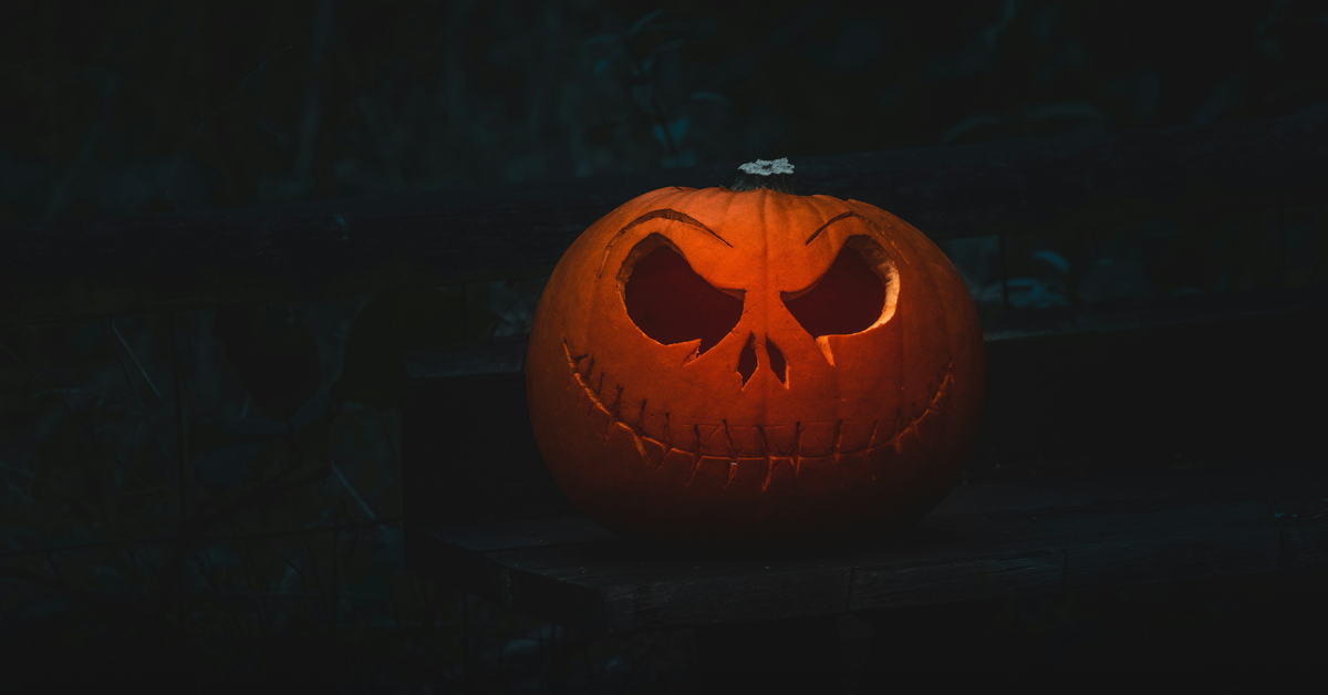 An illuminated jack o' lantern sits against a dark fence.