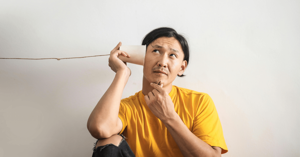 a man sits with his ear to a cup on a string hoping to hear a response.